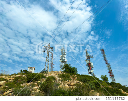 Communication towers and power lines stand tall against a blue sky with scattered clouds, captured on a sunny day in a rural area 131155782