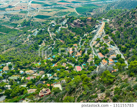 Stunning aerial view of a serene village nestled in lush greenery with a historic castle overlooking the landscape during a bright sunny day Stunning aerial view of a serene village nestled in lush greenery with a historic castle overlooking the landscape during a bright sunny day 131155783
