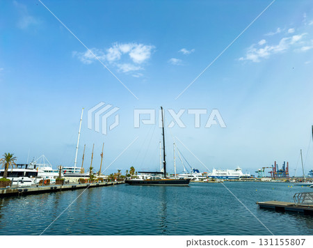 Sailboats and yachts gently sway in the harbor under a sunny sky with fluffy clouds above Sailboats and yachts gently sway in the harbor under a sunny sky with fluffy clouds above 131155807