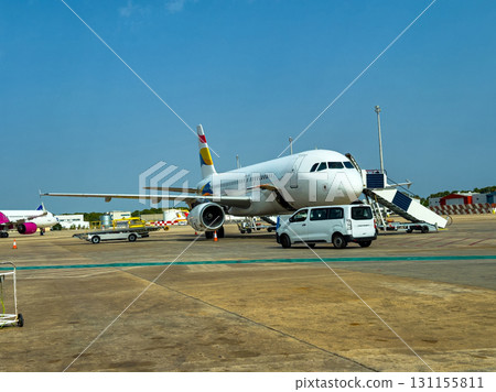 Airplane parked on tarmac at a busy airport with service vehicles and clear blue sky in the background during daytime 131155811
