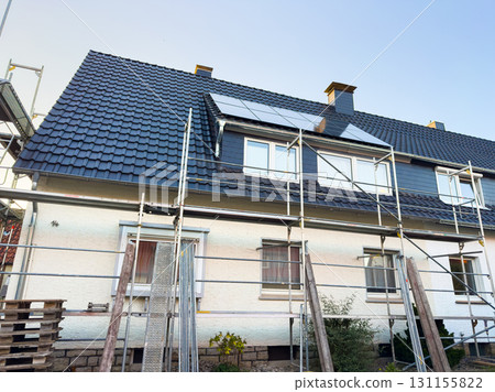 Roof renovation occurs on a residential building with scaffolding in a suburban neighborhood during daylight hours 131155822