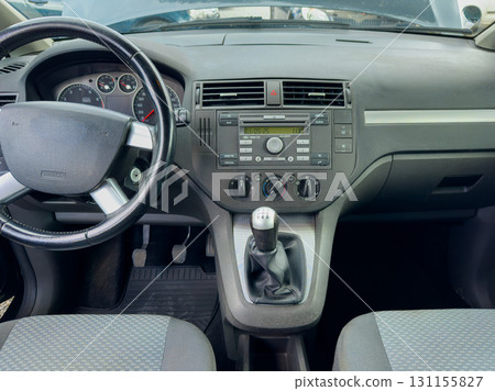 Interior view of a modern vehicle showing steering wheel, dashboard and gear shifter in a clean, organized setting during daytime 131155827