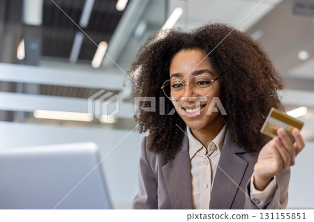 Close-up photo of a young African-American woman working in an office using a laptop, using a credit card in her hand. 131155851