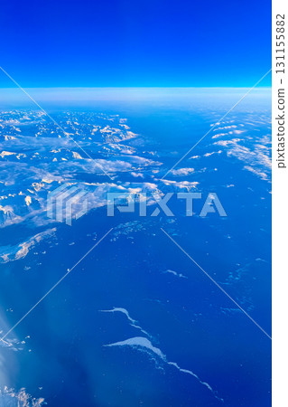 Stunning aerial view of snow-covered mountains and tranquil blue ocean under bright sky at midday Stunning aerial view of snow-covered mountains and tranquil blue ocean under bright sky at midday 131155882