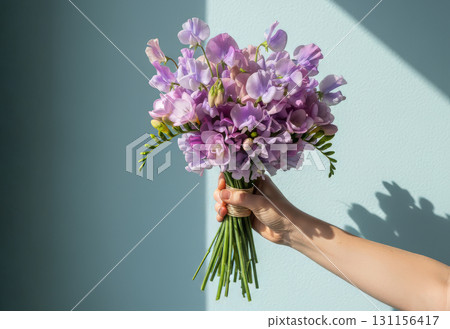 A hand holds a beautiful, elegant bouquet of fresh flowers against a bright, light blue background A hand holds a beautiful, elegant bouquet of fresh flowers against a bright, light blue background 131156417