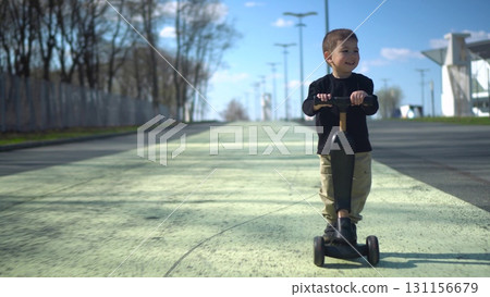 A child joyfully riding their scooter on a sunny day in a beautiful park filled with nature 131156679