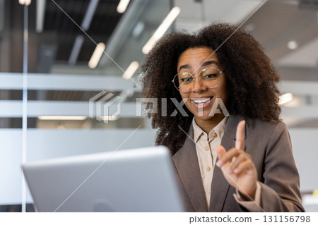 African American young business woman in suit and glasses sitting at office desk and talking on video call on laptop. 131156798