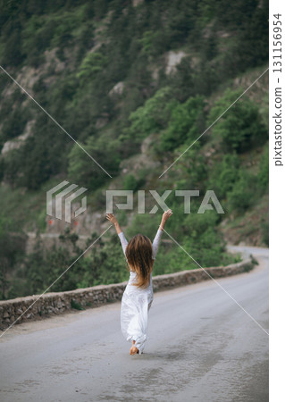 A woman is walking on a road with her arms raised in the air. Concept of freedom and joy, as the woman is celebrating or expressing her happiness. A woman is walking on a road with her arms raised in the air. Concept of freedom and joy, as the woman is celebrating or expressing her happiness. 131156954