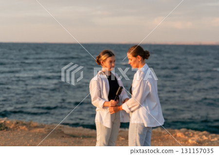 Couple Sunset Beach Romance - Two people holding hands on a cliff overlooking the ocean at sunset. 131157035
