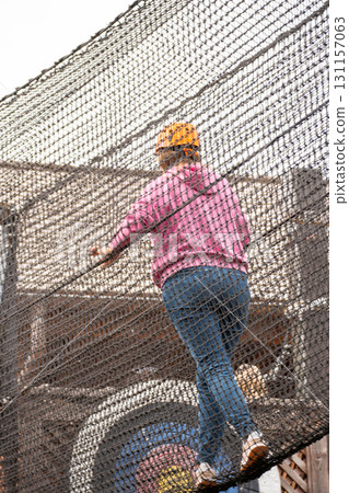 Woman Net Climbing Outdoor Adventure Park - A woman climbs on a net at an outdoor adventure park. Woman Net Climbing Outdoor Adventure Park - A woman climbs on a net at an outdoor adventure park. 131157063