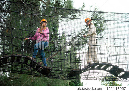 Adventure Park Couple Rope Bridge Two people in hard hats walk across a rope bridge at an outdoor adventure park. 131157067