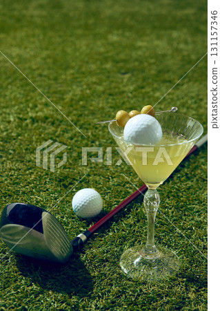 Close up of martini cocktail with golf ball and olives on grass field Close up of martini cocktail with golf ball and olives on grass field 131157346