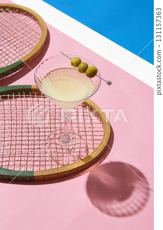 Martini glass with olives on vintage tennis racket over pink surface 131157363