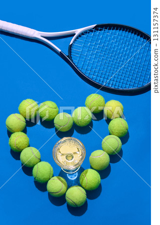 Heart of tennis balls with champagne glass and racket on blue background Heart of tennis balls with champagne glass and racket on blue background 131157374