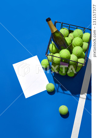 Champagne bottle in basket with green tennis balls on court next to white copy space sheet 131157377