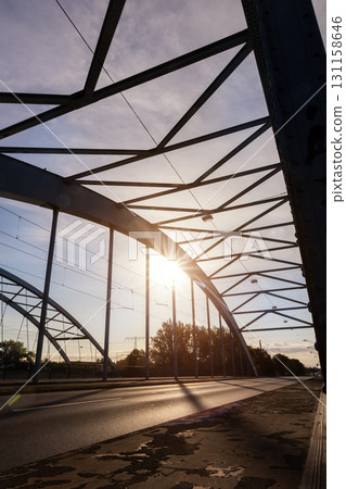 Scenic dynamic view of Magdeburg steel arch Jerusalem bridge cars crossing under warm sunrise sunlight. Urban composition highlights architectural structure traffic movement modern city atmosphere Scenic dynamic view of Magdeburg steel arch Jerusalem bridge cars crossing under warm sunrise sunlight. Urban composition highlights architectural structure traffic movement modern city atmosphere 131158646