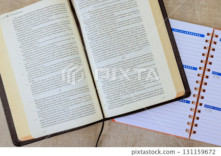An open Bible book sits next to planner on desk, creating thoughtful environment for organization, study. 131159672