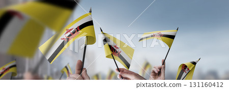 Brunei flags in their hands on a blurred urban background Brunei flags in their hands on a blurred urban background 131160412
