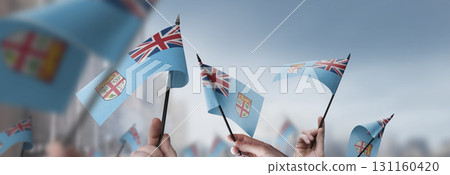 Fiji flags in their hands on a blurred urban background 131160420