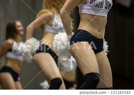 Group cheerleader in black fishnet tights and shorty shorts with white pompoms in her hands Group cheerleader in black fishnet tights and shorty shorts with white pompoms in her hands 131161581