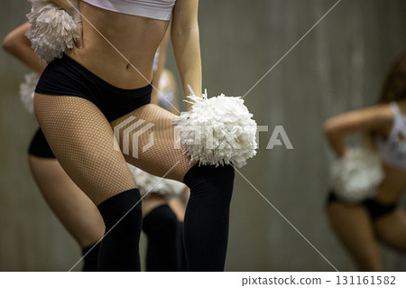 Cheerleader girl in black fishnet tights and shorty shorts with white pompoms in her hands 131161582