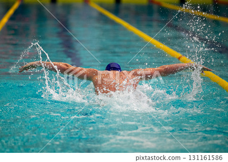 Rear view swimmer performing butterfly stroke at swimming competition Rear view swimmer performing butterfly stroke at swimming competition 131161586