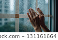 A person holding their hand against a window indoors on a rainy night 131161664