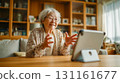 An elderly woman making a video call on a tablet in the living room at home during the day 131161677
