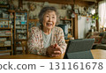 An elderly woman is having a conversation using a tablet in her living room at home during the day 131161678