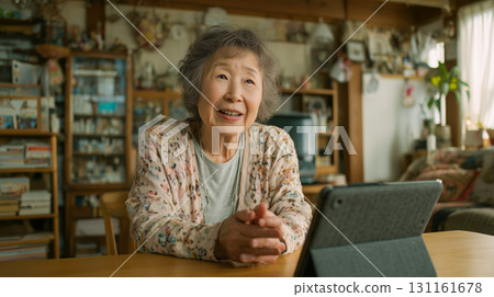 An elderly woman is having a conversation using a tablet in her living room at home during the day 131161678