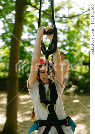 Girl on zipline rope course with helmet and safety harness, outdoor climbing activity Girl on zipline rope course with helmet and safety harness, outdoor climbing activity 131162100