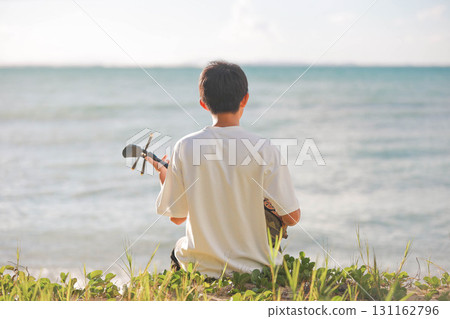 一個男孩在沙灘上彈奏三線琴 一個男孩在沙灘上彈奏三線琴 131162796