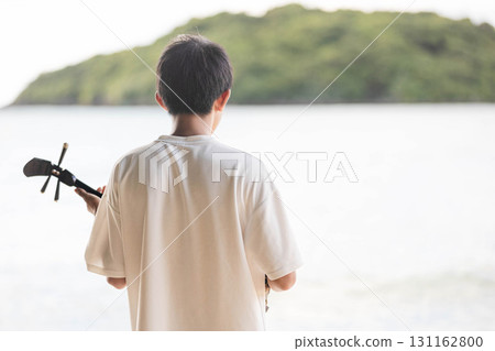 A boy playing the sanshin by the sea 131162800