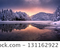 Frozen lake with reflection of snowy forest, colorful sunset sky 131162922