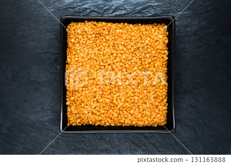 Red Lentil Grains in Black Plate on Black Stone Background Surface with Free Space 131163888
