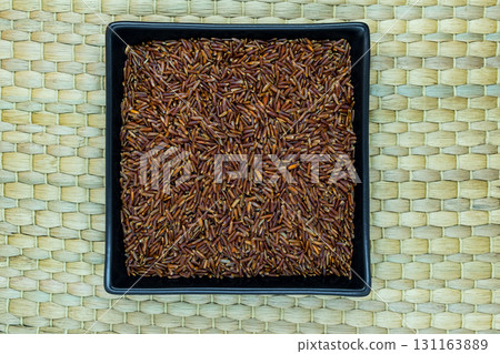 Red Rice Grains in Black Plate on Natural Bamboo Mat Background Surface with Free Space Red Rice Grains in Black Plate on Natural Bamboo Mat Background Surface with Free Space 131163889