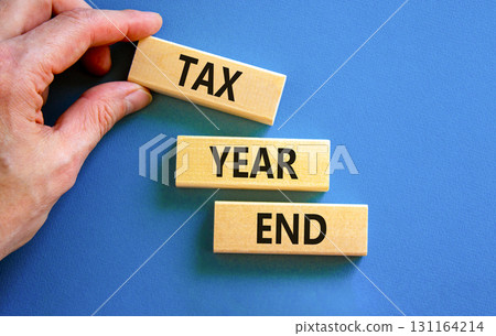Tax year end symbol. Concept words Tax year end on beautiful wooden blocks. Beautiful blue background. Businessman hand. Business tax year end concept. Copy space. Tax year end symbol. Concept words Tax year end on beautiful wooden blocks. Beautiful blue background. Businessman hand. Business tax year end concept. Copy space. 131164214