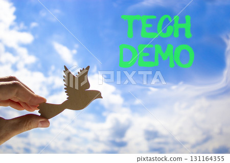 Tech demo symbol. Concept word Tech demo on beautiful blue sky. Businessman's hand with wooden bird. Beautiful blue sky and cloud background. Business tech demo concept. Copy space. 131164355