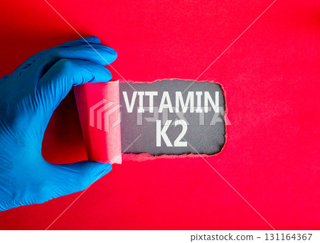 Vitamin K2 phylloquinone symbol. Concept words Vitamin K2 on beautiful grey paper. Doctor hand, blue medical glove. Beautiful red background. Medical healthy lifestyle Vitamin K2 phylloquinone concept 131164367