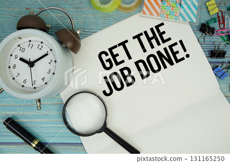 Get The Job Done! text on a paper surrounded by office supplies, a magnifying glass, and a clock on a blue wooden surface 131165250