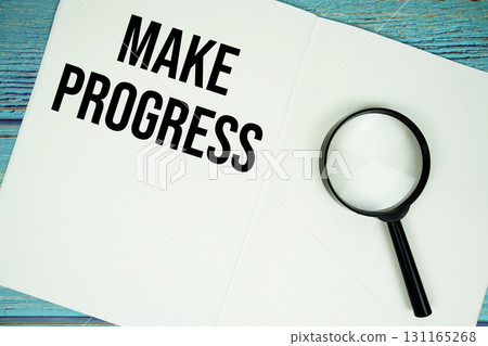 Make Progress text written on notepad with magnifying glass flat lay on wooden background 131165268