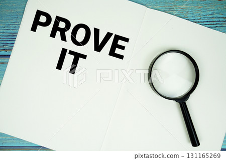 Prove It text written on notepad with magnifying glass flat lay on wooden background 131165269