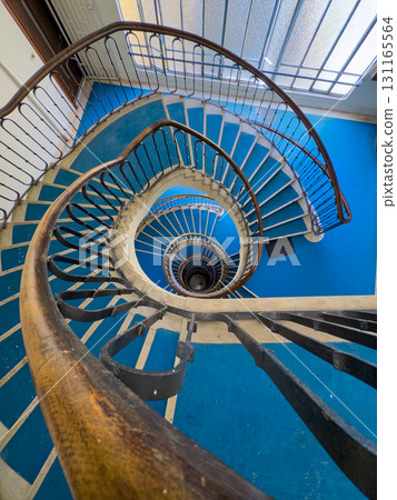 Spiral blue staircase viewed from above with ornate railings and circular descent 131165564
