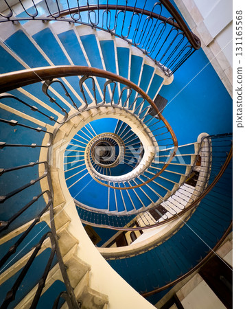 Spiral blue staircase viewed from above with ornate railing creating circular architectural pattern Spiral blue staircase viewed from above with ornate railing creating circular architectural pattern 131165568