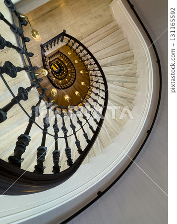 Spiral staircase view from above with ornate black railing and warm lighting interior Spiral staircase view from above with ornate black railing and warm lighting interior 131165592