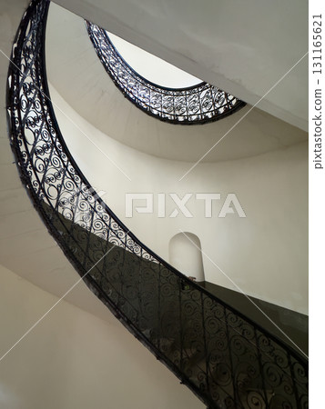 Spiral staircase with ornate wrought iron railing in white interior 131165621