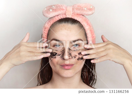 Caucasian woman does a black peel, a cosmetic face mask after a shower. Woman enjoys facial skin care by applying black peel. Woman with pigmentation, melasma, freckles. Close up portrait photo Caucasian woman does a black peel, a cosmetic face mask after a shower. Woman enjoys facial skin care by applying black peel. Woman with pigmentation, melasma, freckles. Close up portrait photo 131166256