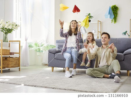 Parents and daughter playing with paper planes in cozy home living room together Parents and daughter playing with paper planes in cozy home living room together 131166910