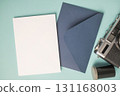 Empty white blank greeting or invitation card, envelope, vintage camera and film box on blue background. 131168003