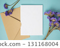 Empty white blank greeting or invitation card with envelope and violet flower decoration on blue background. 131168004